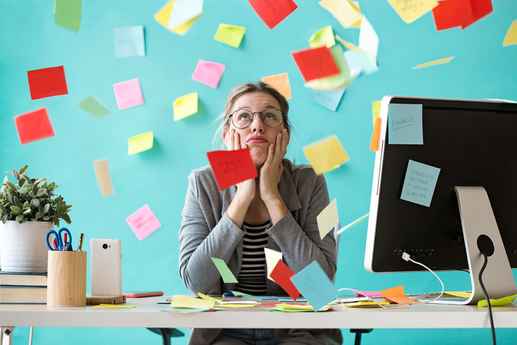 stressed young woman working at a computer desk with sticky notes placed everywhere